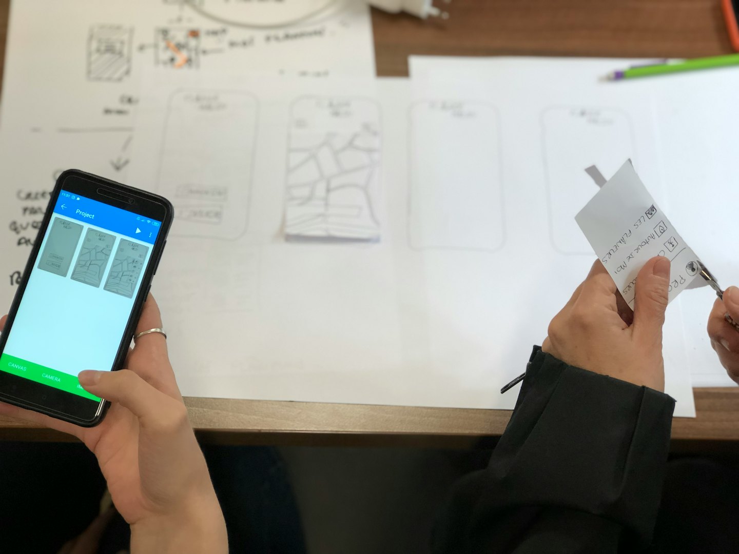 Dłonie pracujące nad projektem aplikacji ze szkicami i smartfonem.